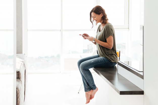 Uma mulher sentada em um balcão segurando seu smartphone e sendo impactada por um SMS marketing.